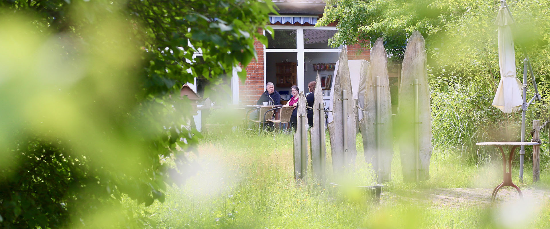 Drei Menschen aus dem Betreuten Wohnen sitzen im Garten ab einem Tisch vor der Terrassentür